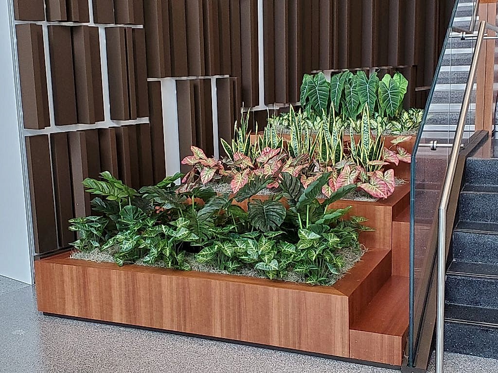 Wood planter with tropical plants and tulips near an office atrium staircase