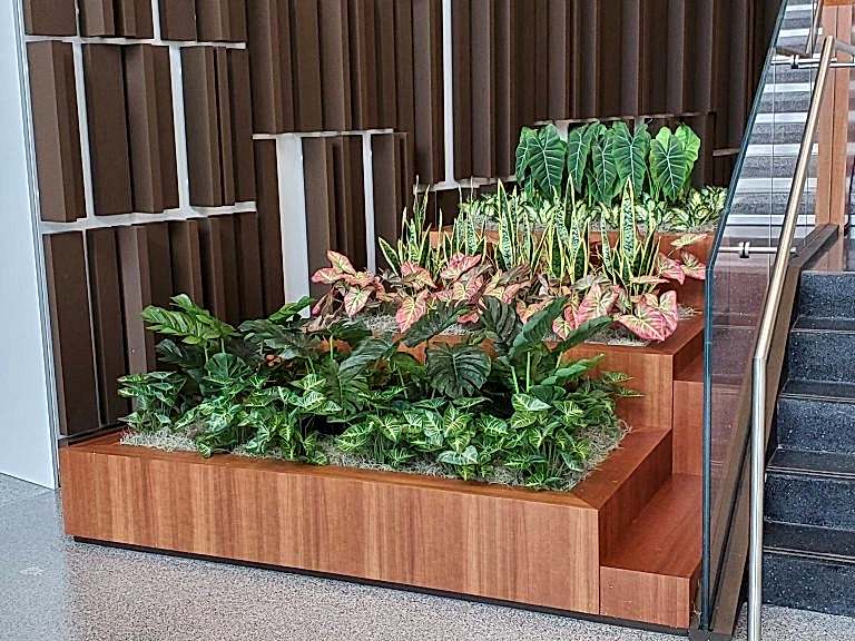 Wood planter with tropical plants and tulips near an office atrium staircase